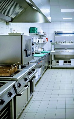 A commercial kitchen cooking devices, stoves and ovens. White tile floor. Stainless steel appliances